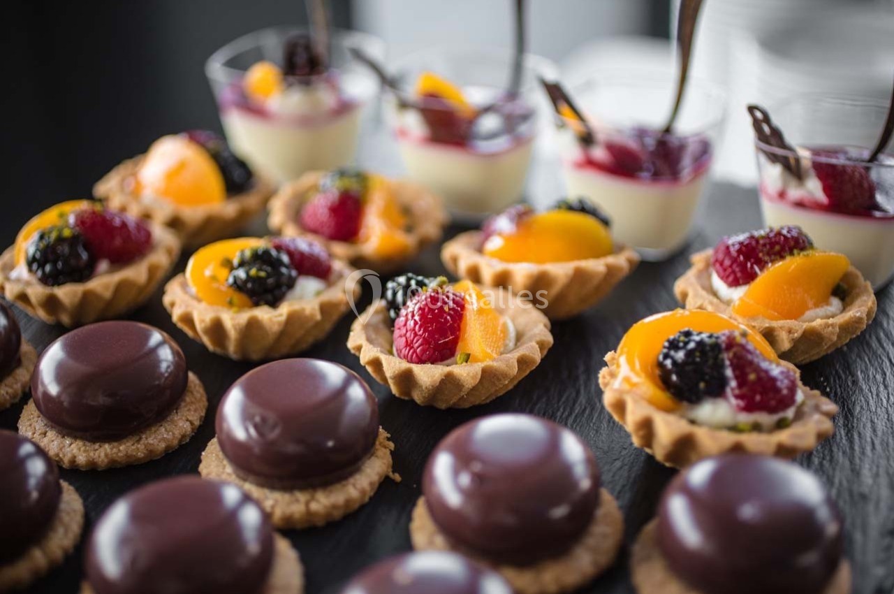 Assortiment de desserts comprenant tartelettes aux fruits, verrines et pâtisseries au chocolat sur une table noire.