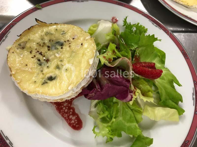 Assiette avec un fromage gratiné accompagné de salade verte, de fruits rouges et d'une sauce.