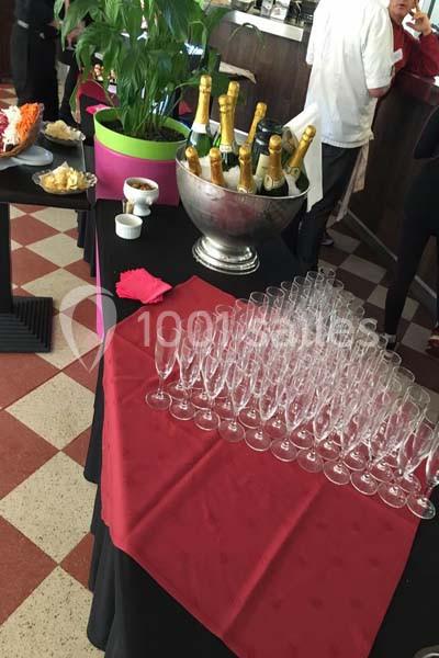 Table dressée avec des flûtes à champagne, un seau rempli de bouteilles et des plantes en arrière-plan.