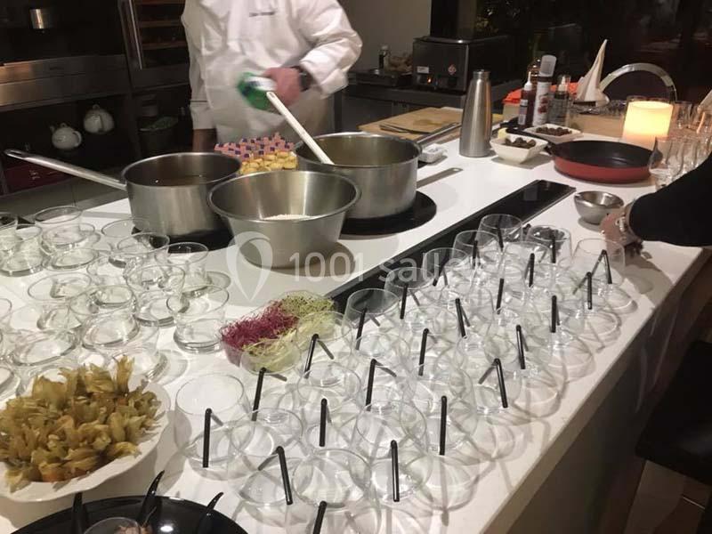 Un chef prépare des plats dans une cuisine avec des bols transparents alignés sur un comptoir.