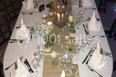 Table décorée pour un dîner, avec nappes blanches, serviettes pliées, lanternes, fleurs et couverts disposés.