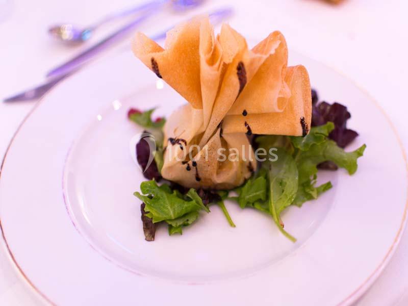 Feuilleté doré présenté sur un lit de salade verte, servi dans une assiette blanche avec des couverts en arrière-plan.