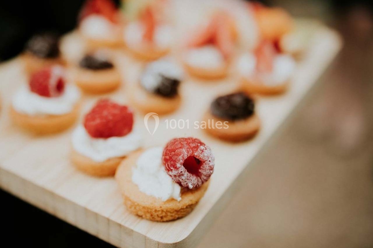 Plateau en bois avec des mini-tartelettes garnies de crème, framboises fraîches et morceaux de chocolat.