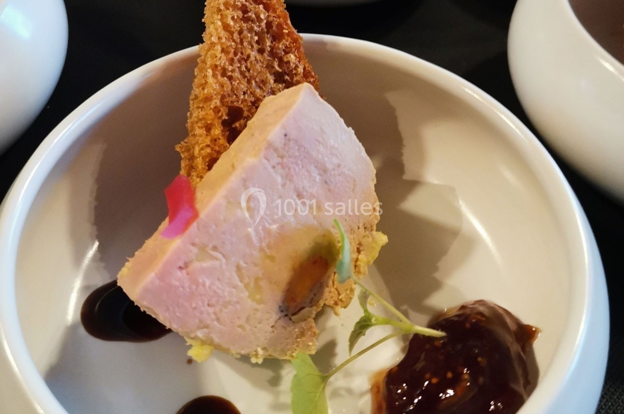 Part de foie gras servie avec une tranche de pain grillé, une sauce brune et une touche de verdure dans une assiette blanche.