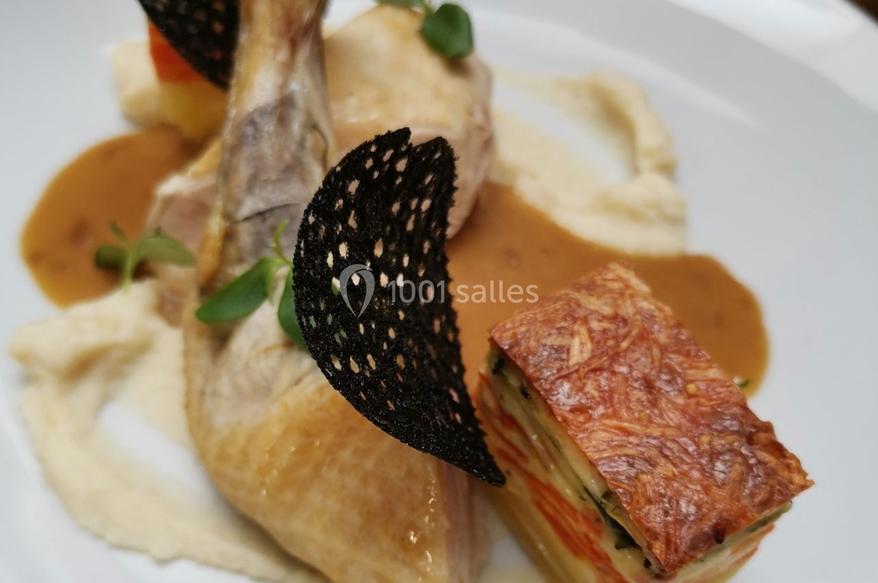 Plat gastronomique composé d'une cuisse de volaille, purée, millefeuille de légumes et sauce, décoré de tuiles noires.
