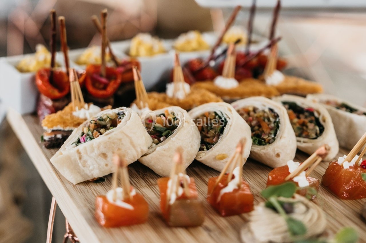 Plateau de bouchées variées comprenant wraps, brochettes et amuse-bouches colorés sur une planche en bois.