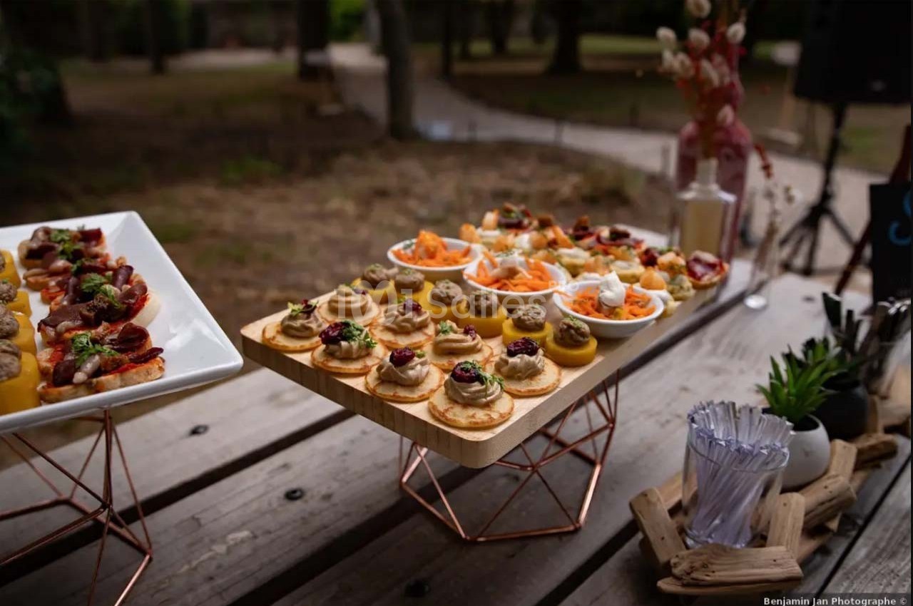 Plateaux de bouchées apéritives variées disposés sur une table en bois dans un cadre extérieur.