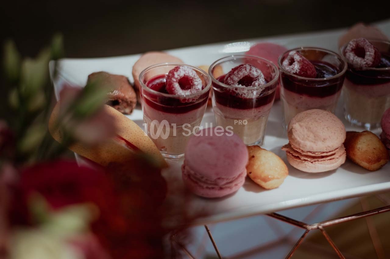 Plateau de desserts comprenant des verrines aux fruits rouges, macarons roses et petites pâtisseries dorées.