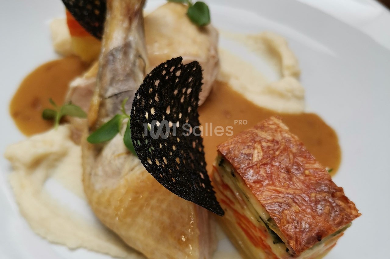 Plat gastronomique composé d'une cuisse de volaille, purée, millefeuille de légumes et sauce, décoré de tuiles noires.