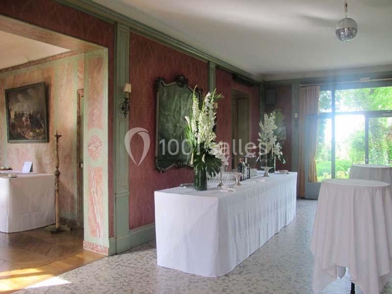 Salle élégante avec table drapée de blanc, décorée de fleurs et baignée de lumière naturelle provenant des fenêtres.
