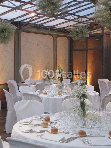 Salle de réception décorée avec des tables rondes dressées, nappes blanches et centres de table floraux.