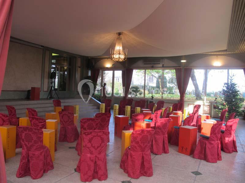 Chaises rouges décorées et tambours colorés disposés dans une salle lumineuse avec vue sur un jardin.
