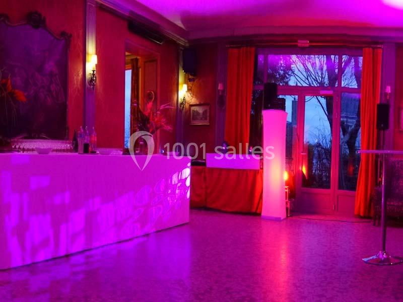 Salle de réception éclairée de lumières violettes, avec un bar, des tables hautes et des rideaux rouges.