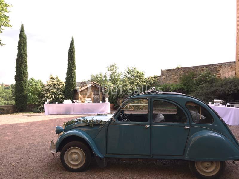 Une voiture ancienne bleue décorée de fleurs est garée dans une cour extérieure près de tables dressées.