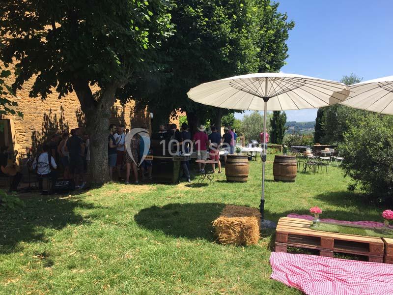 Groupe de personnes rassemblées dans un jardin ombragé avec tables, parasols et décor champêtre.