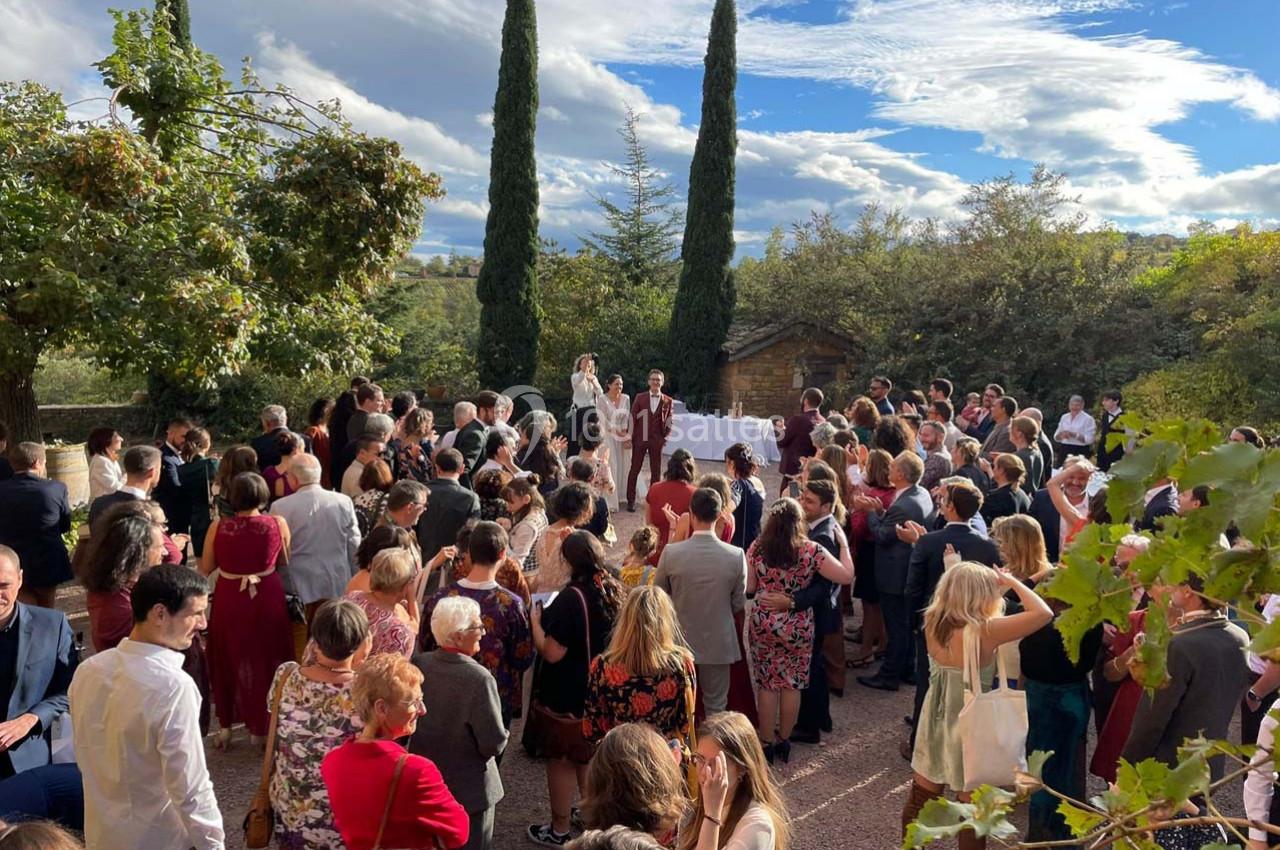 Un groupe de personnes rassemblées en extérieur pour une cérémonie, avec des arbres et un ciel partiellement nuageux en…