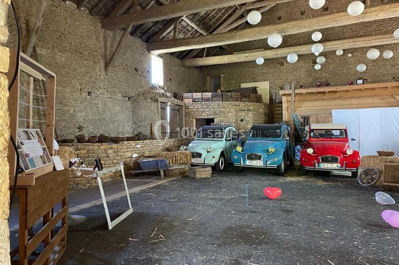 Trois voitures anciennes colorées stationnées dans une grange en pierre avec des décorations suspendues.