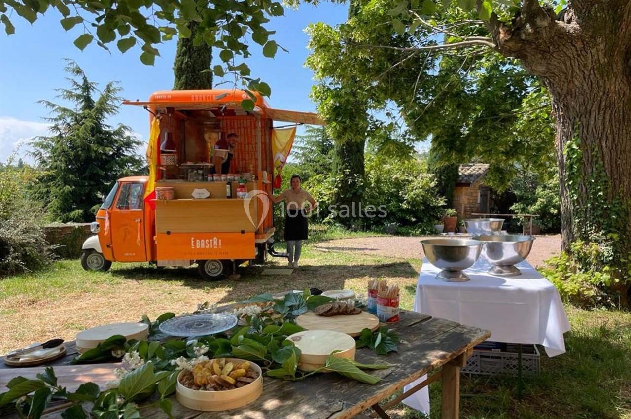 Un food truck orange dans un cadre champêtre avec des tables dressées pour un service en extérieur.