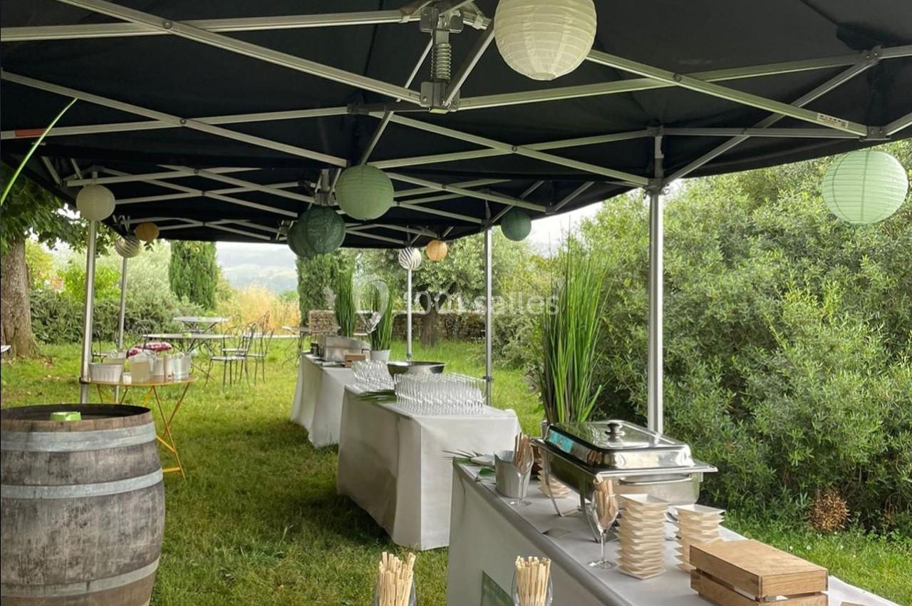Buffet en extérieur sous des tonnelles noires, avec vaisselle, plats et décorations lumineuses dans un cadre verdoyant.