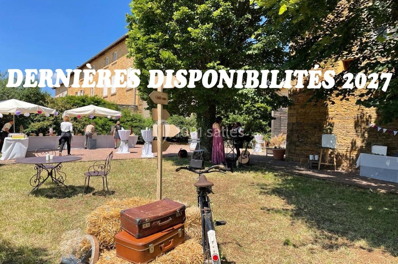 Jardin ensoleillé avec tables décorées, vélo posé sur une botte de paille et panneaux indiquant un événement festif.