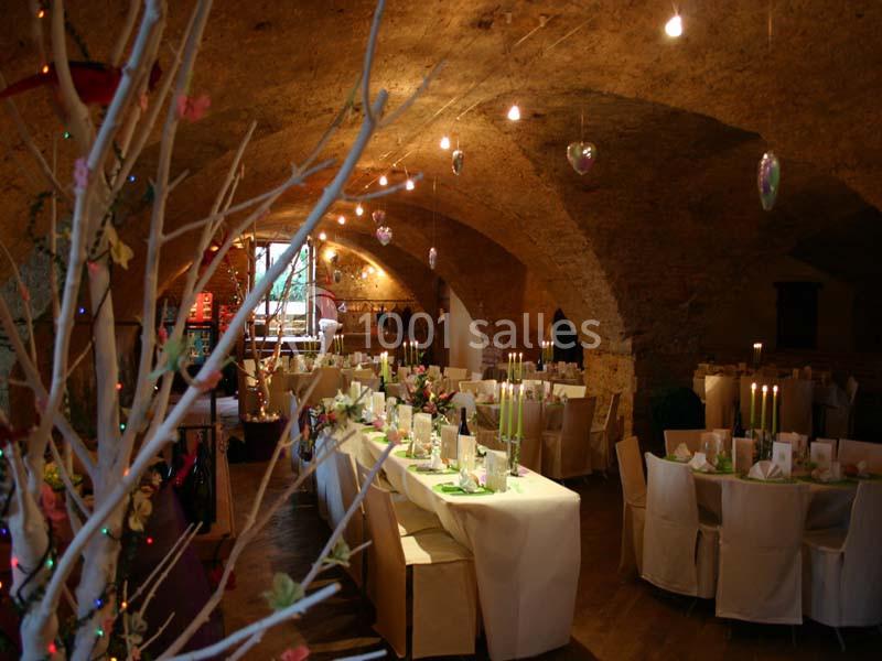 Salle voûtée décorée pour un événement, avec tables dressées, chaises blanches et éclairage tamisé.
