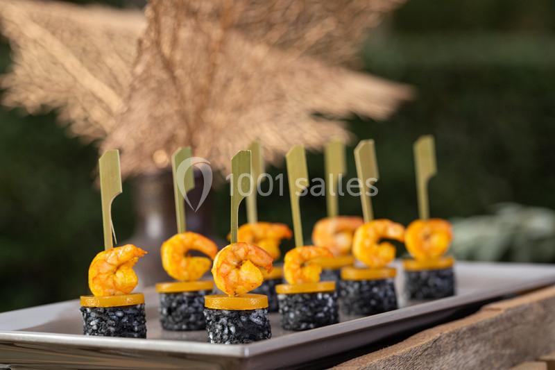 Brochettes apéritives avec crevettes grillées, rondelles de poivron et base de riz noir, présentées sur un plateau.