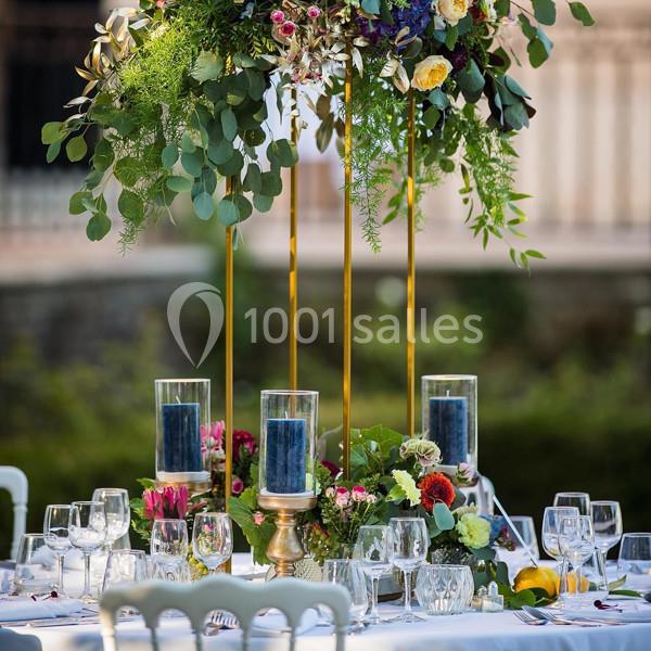 Table décorée pour un événement avec bougies, fleurs colorées et feuillage, disposée en extérieur.