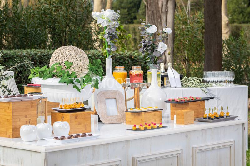 Buffet en plein air avec verrines, amuse-bouches, boissons et décorations florales sur une table blanche.