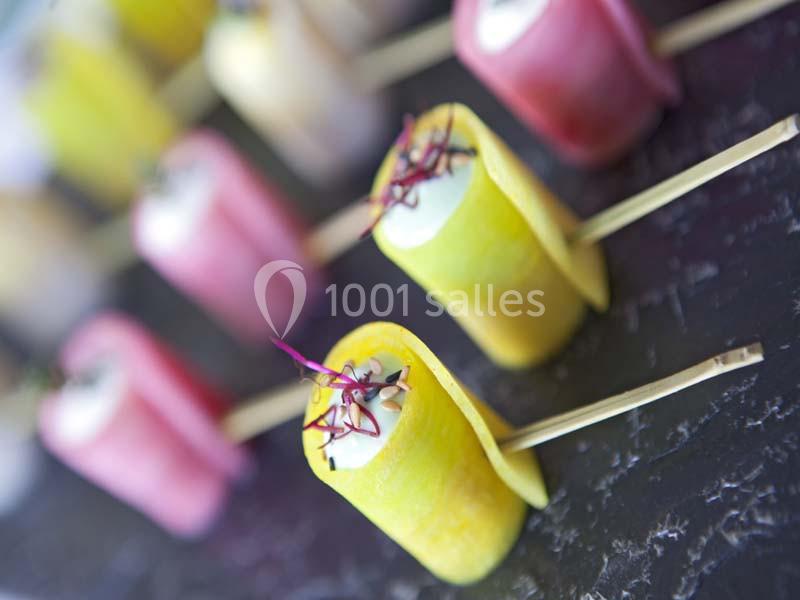 Bouchées colorées enroulées dans des tranches de légumes, présentées sur des piques en bois sur une surface sombre.