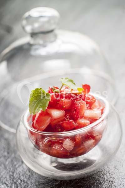 Salade de fraises fraîches servie dans une verrine, décorée de feuilles de menthe sous une cloche en verre.