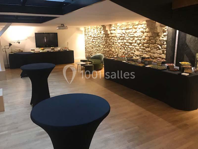 Salle avec parquet, murs en pierre, tables hautes noires et buffet disposé le long d'un mur.