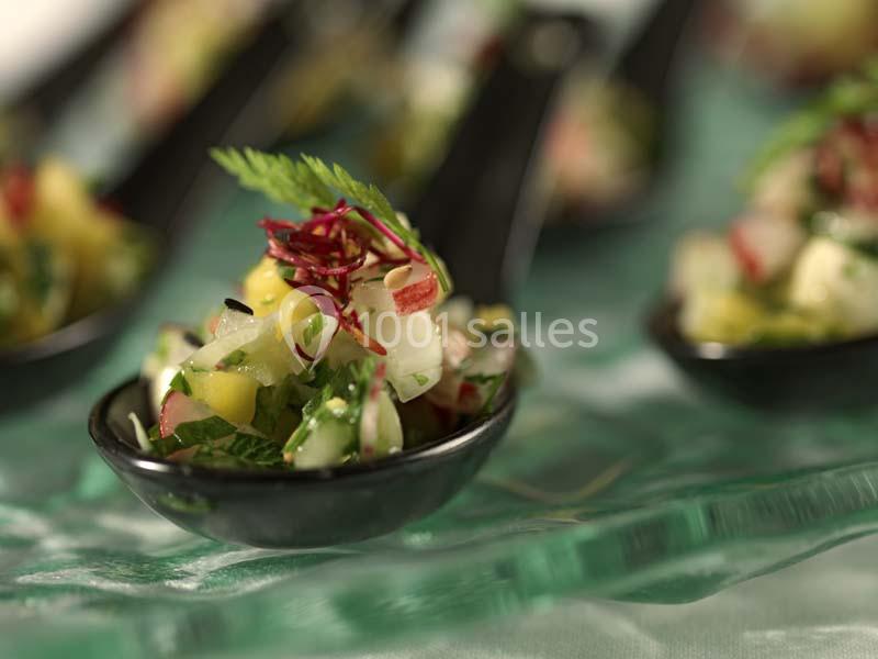 Mélange coloré de légumes et herbes fraîches servi dans une cuillère noire sur une nappe verte.