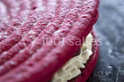 Gros plan sur un macaron rouge garni de crème blanche, posé sur une surface sombre.