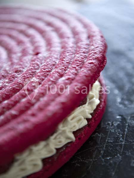 Gros plan sur un macaron rouge garni de crème blanche, posé sur une surface sombre.