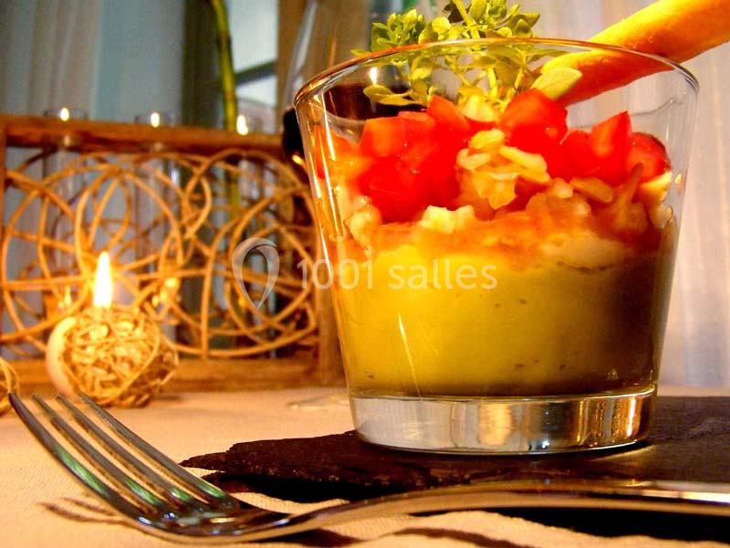 Verrine colorée avec purée d'avocat, dés de tomate, fromage râpé et gressin, posée sur une table décorée.