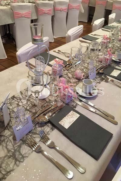Table décorée pour un événement avec nappes blanches, chemins de table en dentelle, bougies et accessoires roses.
