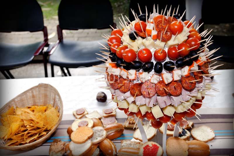 Bouquet de brochettes apéritives avec tomates, fromages, charcuteries et olives, accompagné de snacks sur une table.