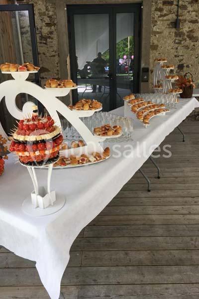 Table de réception avec mignardises, verrines et pièces montées sur nappes blanches, disposée en extérieur couvert.