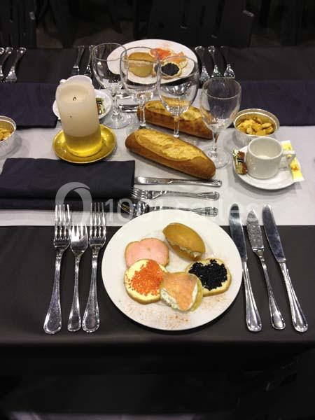 Table dressée avec couverts, assiettes contenant toasts au saumon et caviar, bougie, pain et tasses à café.