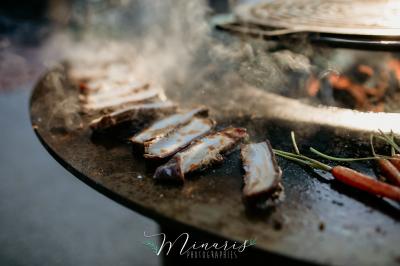 Miniature Traiteur Aubeterre (Aube) - Au Bois du Bon Sejour #16 Un chef cuisine sur un brasero dans un jardin, entouré de tables et de végétation.