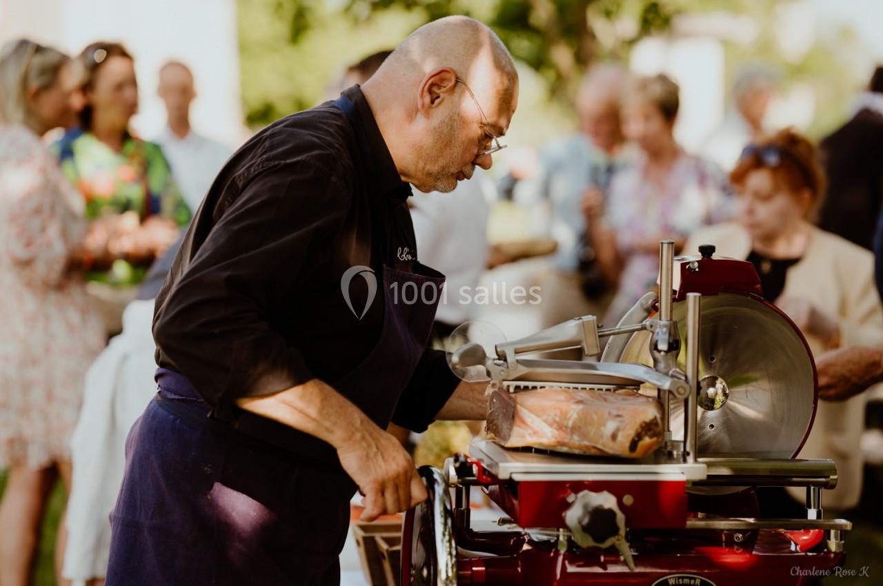 Un homme tranche du jambon sur une machine à découper lors d'un événement en extérieur.
