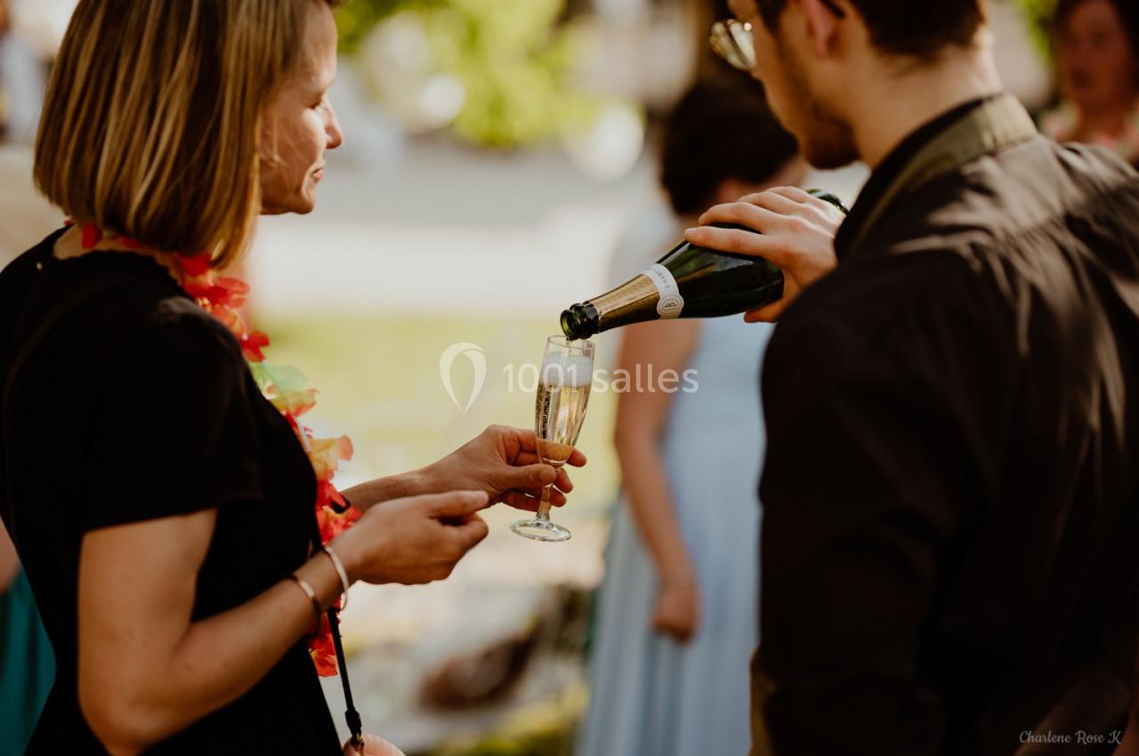 Une personne verse du champagne dans un verre tenu par une autre personne lors d'un événement en extérieur.