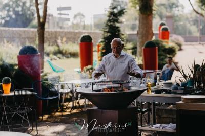 Miniature Traiteur Aubeterre (Aube) - Au Bois du Bon Sejour #18 Un chef cuisine sur un brasero dans un jardin, entouré de tables et de végétation.
