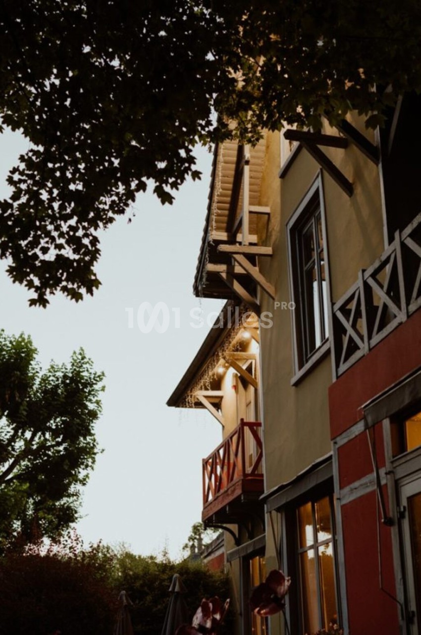 Façade d'une maison colorée au crépuscule, entourée d'arbres et de végétation.