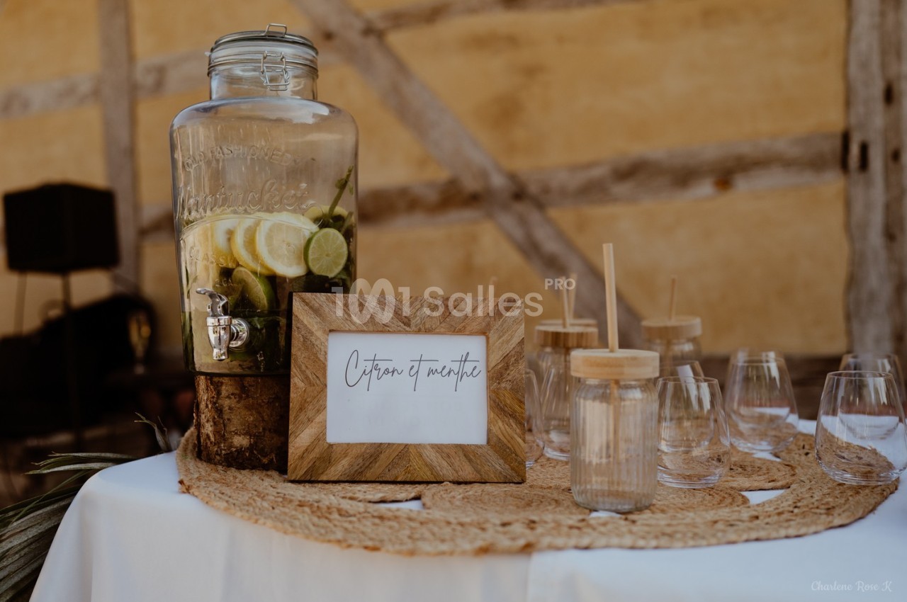 Distributeur de boisson citron-menthe avec verres et pailles en bois sur une table décorée.