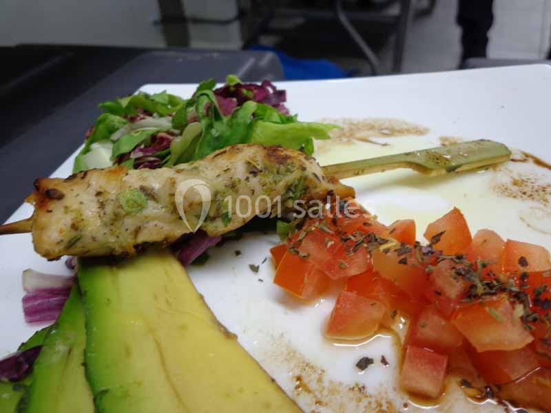 Brochette de poulet grillé avec avocat, dés de tomate assaisonnés et salade verte sur une assiette blanche.