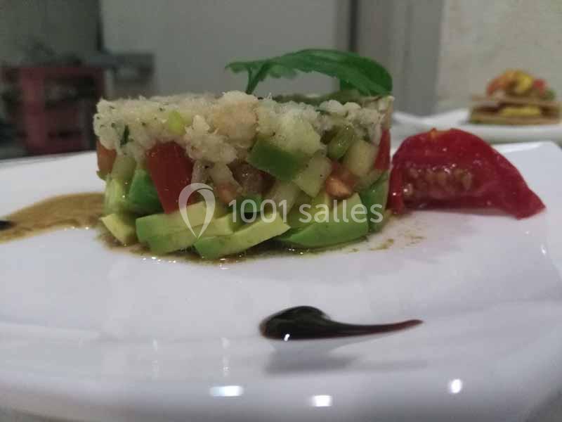 Tartare de légumes frais avec avocat, tomate et basilic, présenté sur une assiette blanche avec une sauce décorative.