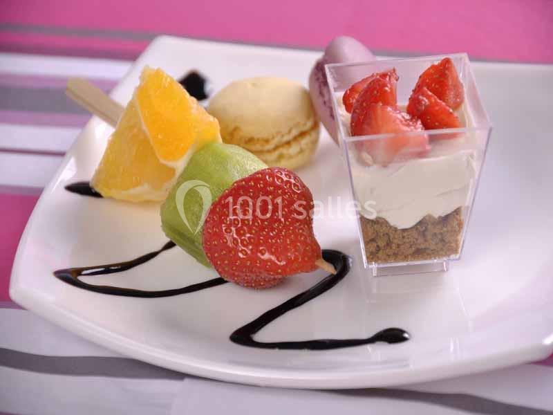 Assortiment de desserts comprenant brochette de fruits, macaron, verrine aux fraises et coulis de chocolat.