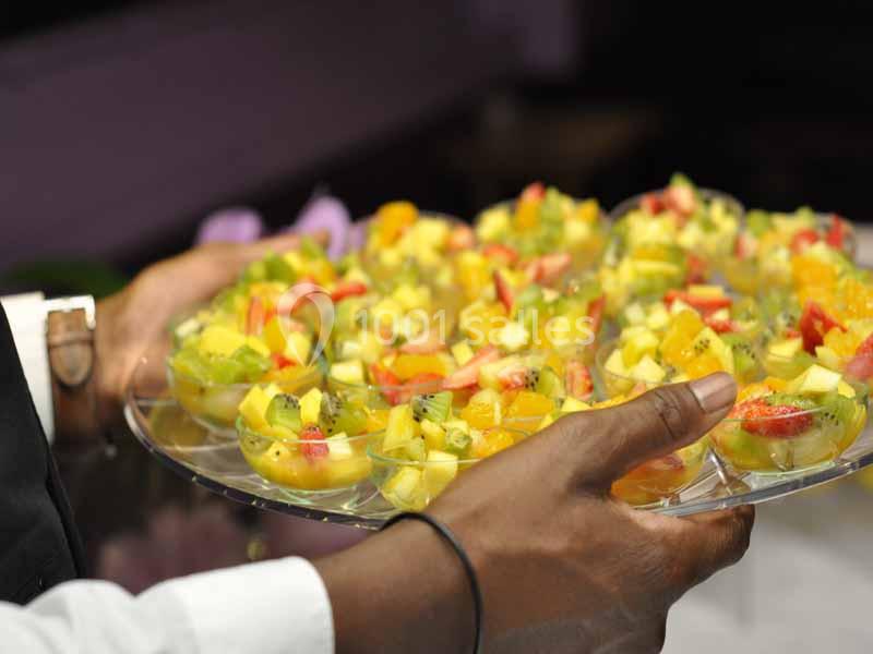 Plateau de verrines colorées garnies de fruits frais comme kiwi, fraise et mangue, tenu par une personne.