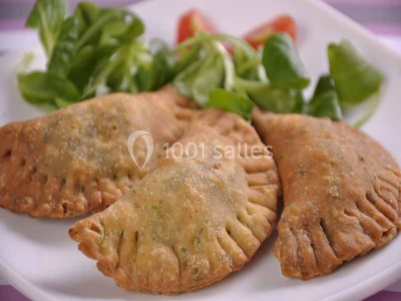 Trois empanadas dorées servies avec une salade verte et des morceaux de tomate sur une assiette blanche.